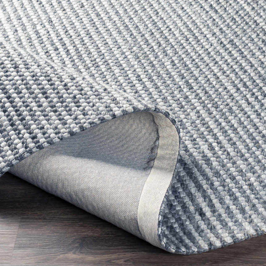 Close-up of the hand woven Mulgoa Area Rug. The rug is medium gray with a textured, contemporary design. Fold