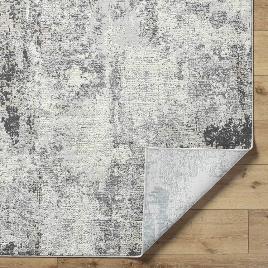 Close-up of the Marci Area Rug showing a charcoal, cream, and gray abstract pattern on a wood floor. Southwestern style. Fold