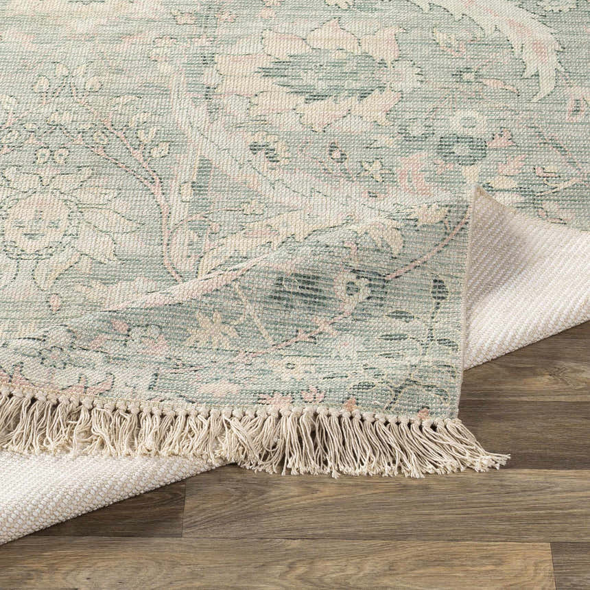 Close-up of the Enderby rug. Handwoven cotton-blend rug in dark green, light pink floral pattern with fringe detail. Fold