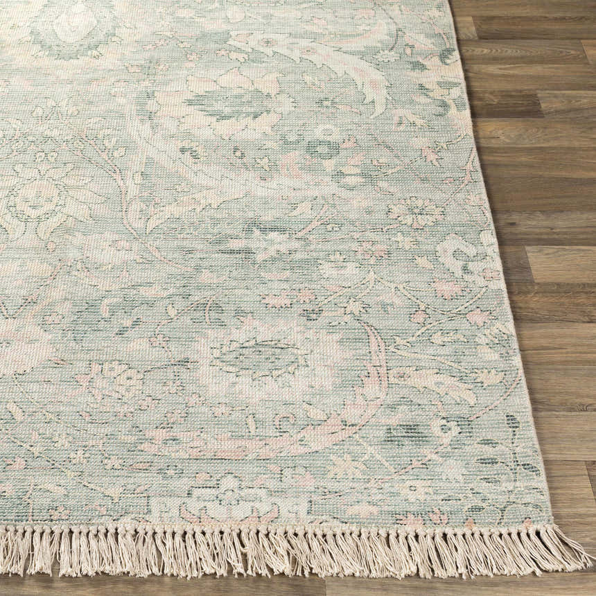 Close-up of the Enderby Handmade Cotton-blend Rug. Features a green, pink, and white floral pattern and fringe detail. Front
