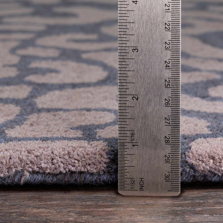 Close-up of the gray Neoma Animal Print Wool Rug showing its texture and pile height with a ruler. Pile