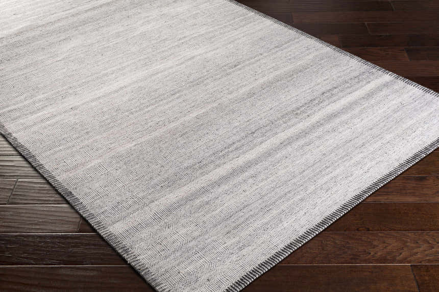 Close-up of Nettleham Silver Viscose Rug showing woven texture and charcoal, gray, and silver tones on dark wood floor. Corner
