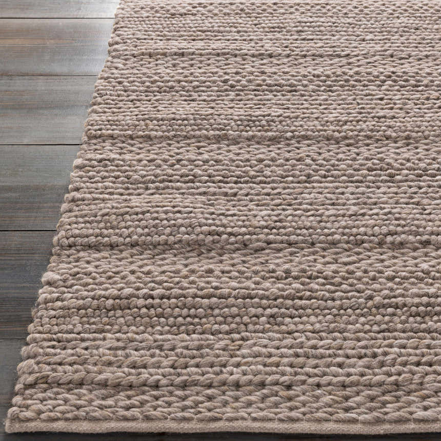 Close-up of the hand woven Newfolden Area Carpet, brown and ivory wool texture on gray wood floor. Front