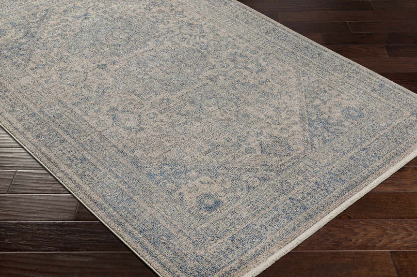 Close-up of the Nira Area Rug, a traditional design in dark blue, ivory, and light gray on a dark wood floor. Corner