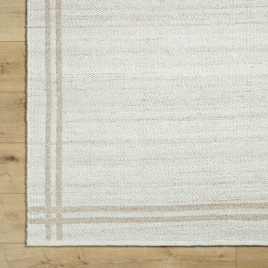 Close-up of the hand-woven Nimue Area Rug. Ivory and tan wool rug with a simple border design. Farmhouse style. Corner
