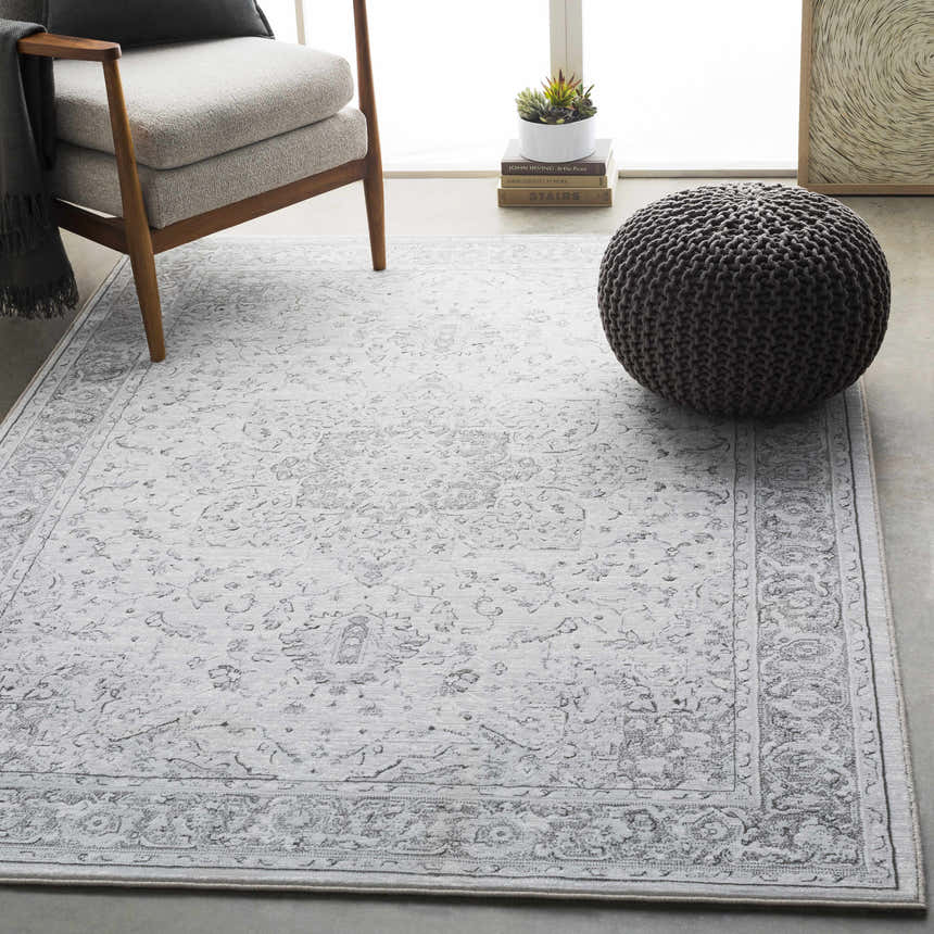 Living room scene with a light gray Okehampton Area Rug, charcoal pouf, and modern chair. Roomscene-Rectangle