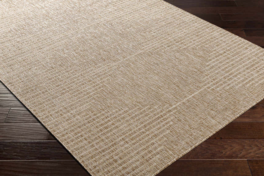 Close-up of the woven texture and dark beige color of the Stephan Dark Beige Outdoor Rug on dark wood flooring. Corner