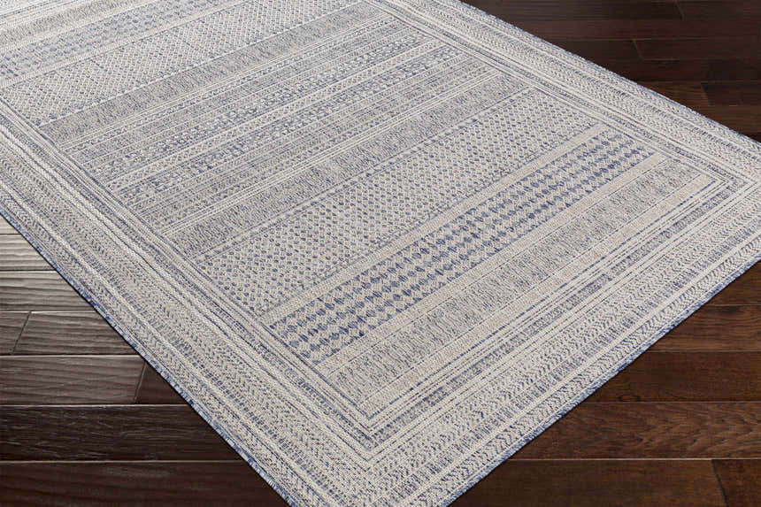 Close-up of the Panaytayon Area Rug showing a contemporary geometric pattern in cream and navy on dark wood floors. Corner