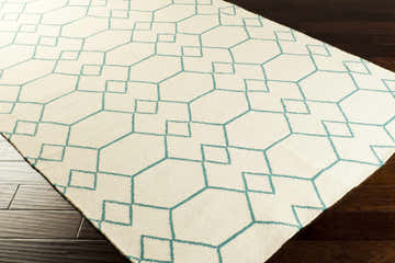 Close-up of the Paonia Area Rug. Beige wool rug with a geometric teal pattern on dark wood floors. Corner