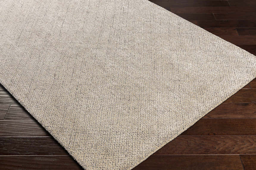 Close-up of the Phalaborwa Area Rug, a hand-loomed contemporary rug in gray, light beige, and tan, on a dark wood floor. Corner