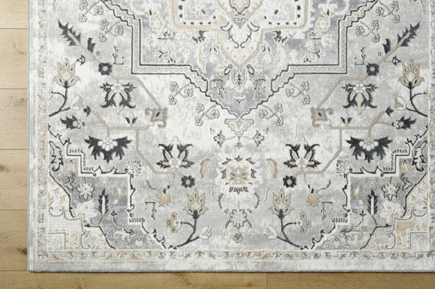 Close-up of the Phyre Area Rug. Light gray rug with traditional floral pattern in gray, black, and beige on wood floor. Corner