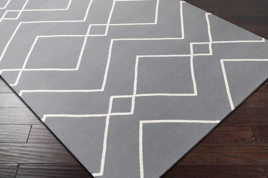 Close-up of the Pinewood Area Rug. Gray rug with an off-white geometric pattern on dark wood floors. Corner