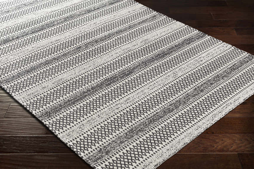 Close-up of the Planada Washable Area Rug. Black and cream cotton rug with a bohemian geometric pattern on dark wood floors. Corner