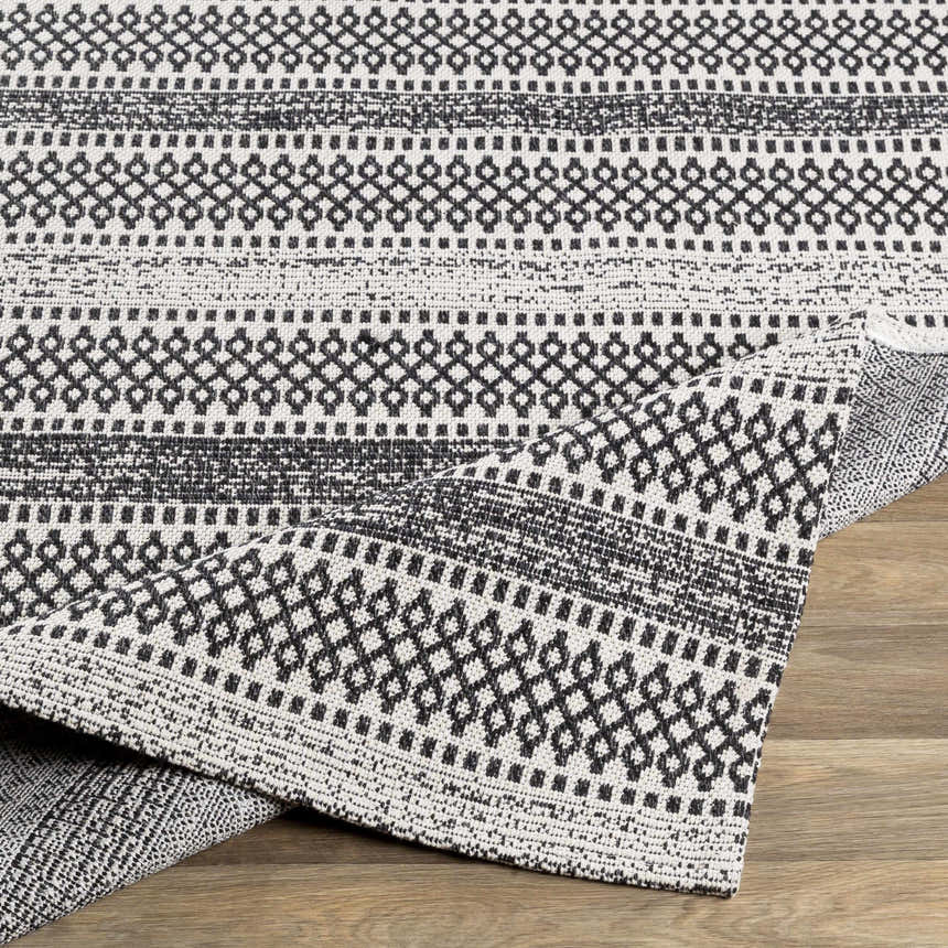 Close-up of the Planada Washable Area Rug in black and cream, showcasing its woven Bohemian-inspired geometric pattern. Fold