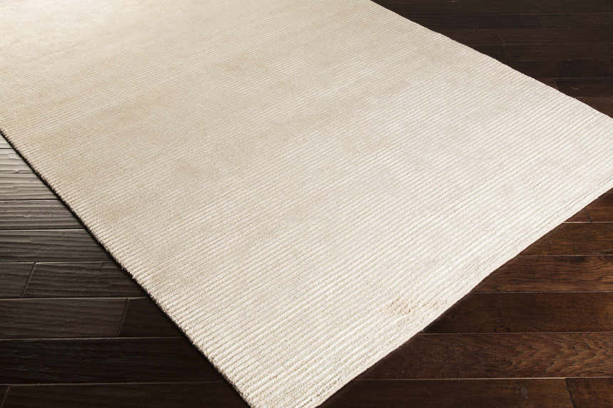 Close-up of the beige Plummer Area Carpet showing its hand woven texture and striped design on dark wood floors. Corner