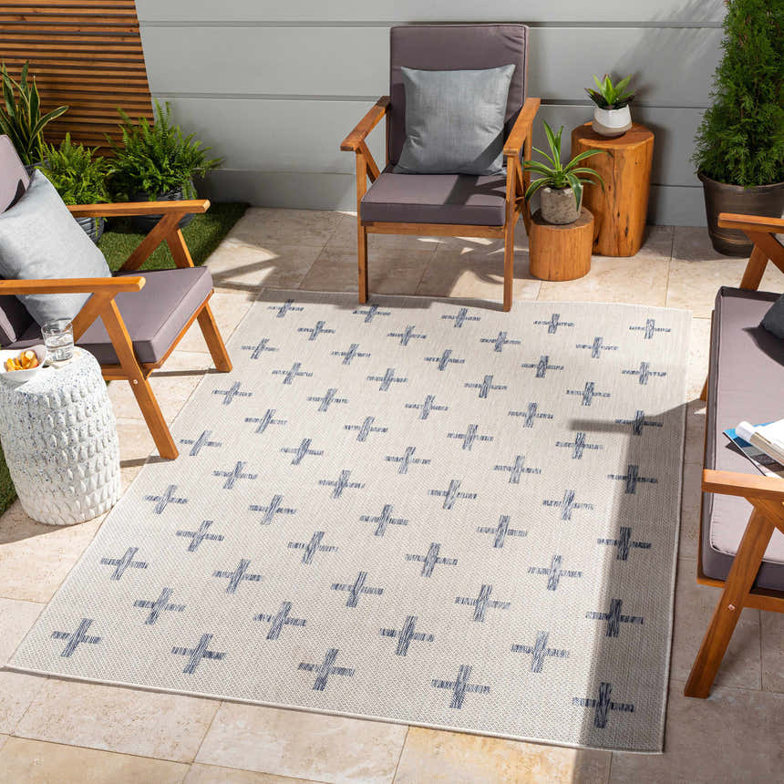 Outdoor patio scene with Pangao Area Rug in cream and navy, geometric pattern, surrounded by wooden chairs and potted plants. Roomscene-Rectangle