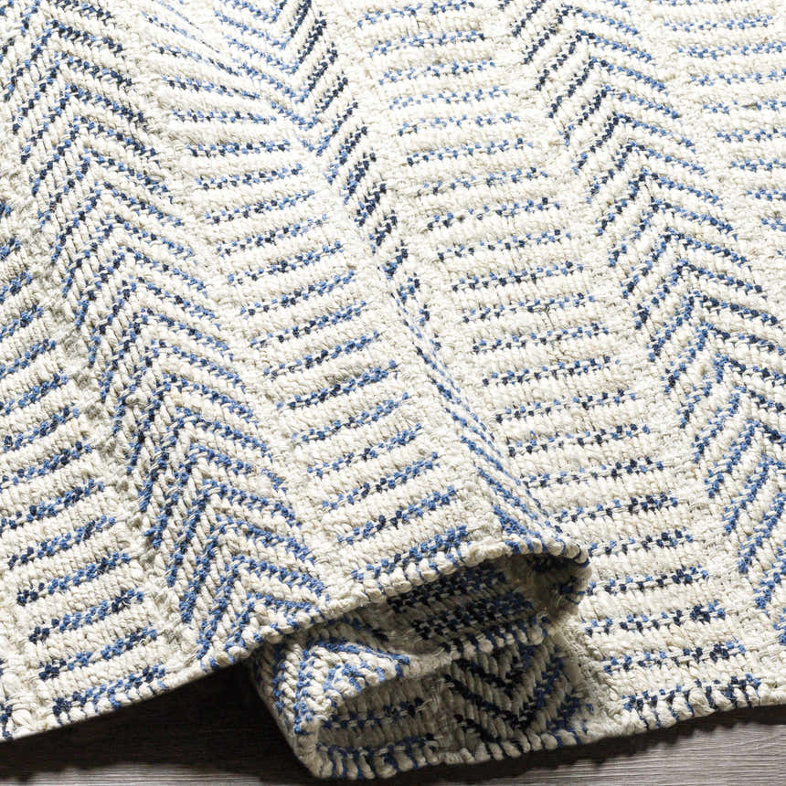 Close-up of the hand woven Pontian Area Rug. Beige jute rug with a contemporary blue and black chevron pattern. Fold