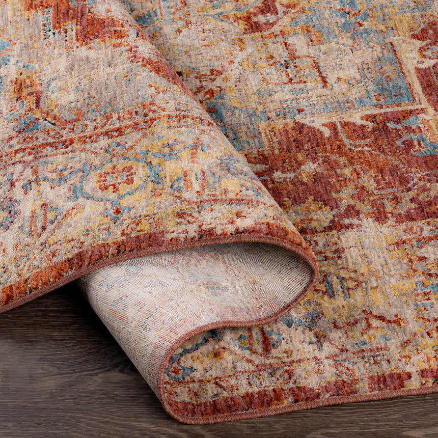 Close-up of the Powassan Area Rug showing its brick red, teal, and beige traditional pattern and soft texture. Fold
