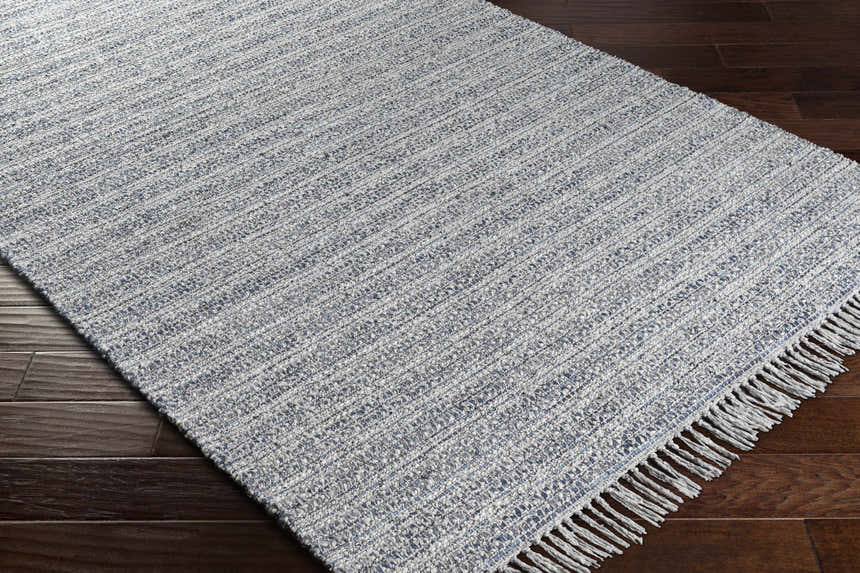 Close-up of the Potterspury Area Rug. Hand-loomed rug in blue, cream, and gray on a dark wood floor. Contemporary style. Corner