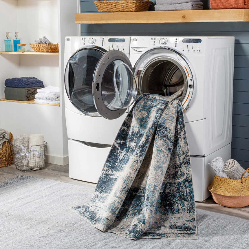 Laundry room scene with the blue and cream Pugo Washable Area Rug coming out of the washing machine. Washing-Machine