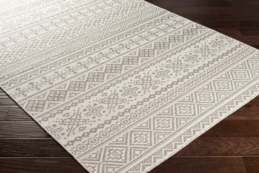 Close-up of the Pumwani Area Carpet. Cream and gray wool rug with a geometric, bohemian-inspired pattern. Hand woven texture. Corner