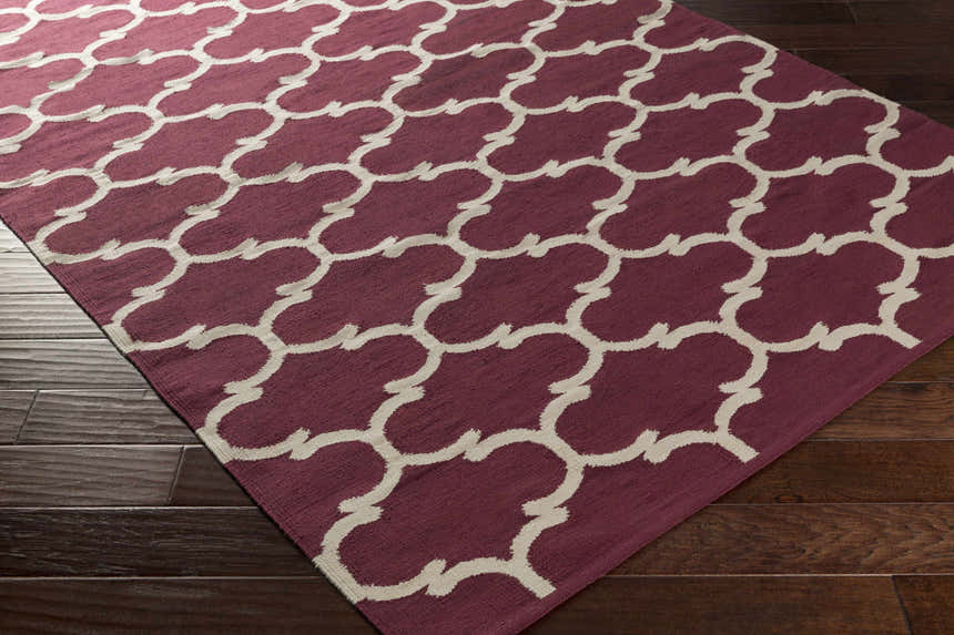 Close-up of the Racine Area Carpet. Dark purple cotton rug with an ivory quatrefoil pattern on a dark wood floor. Corner