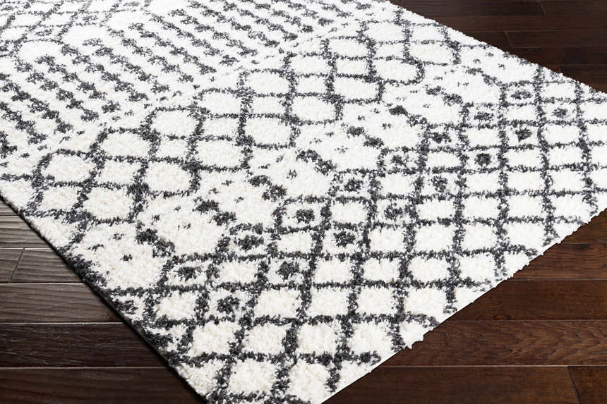 Close-up of the Walkern White/Black 5x7 Plush Rug, showing its geometric shag design and soft texture on dark wood floors. Corner