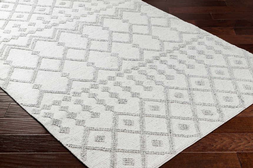 Close-up of the Rick Area Rug showing its geometric pattern and gray and arctic stone colors on dark wood flooring. Corner