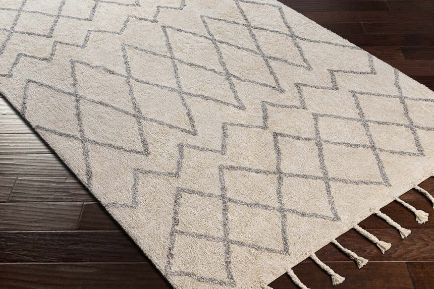 Close-up of the Redlands Area Rug, a cream cotton rug with gray geometric diamond pattern and tassels. Corner