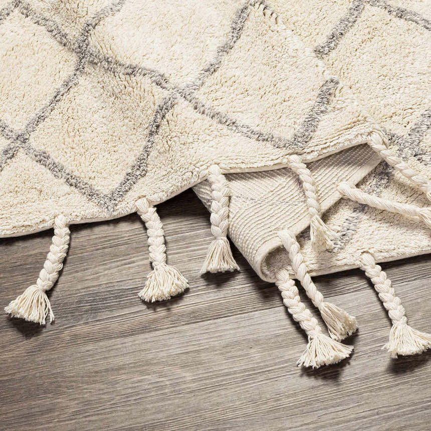 Close up of the cream and gray Redlands area rug, showing its diamond pattern and braided tassels. Fold