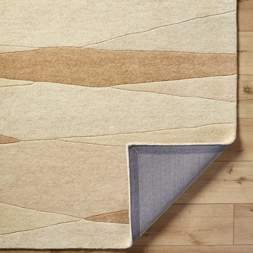 Close-up of the hand-tufted Robin Modern Wool Rug. Caramel and cream abstract design. Rug backing shown. Fold