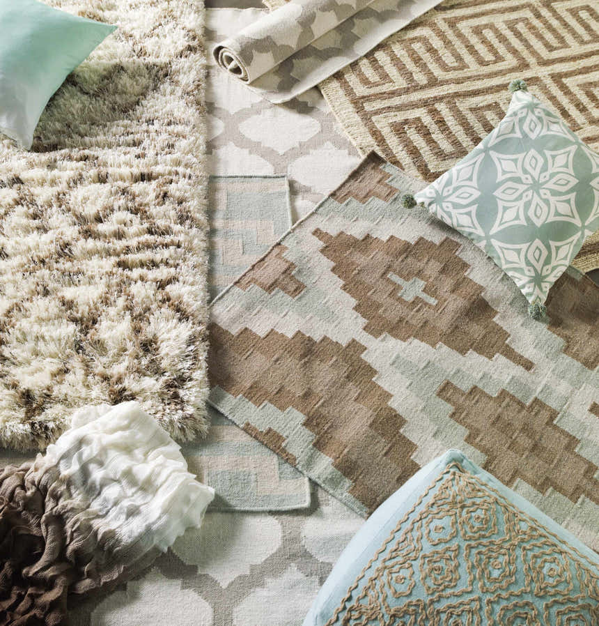 Close-up of various rug designs, including the Banks Ivory/Gray Trellis Wool Rug, with coordinating throw pillows and a blanket. Styleshot