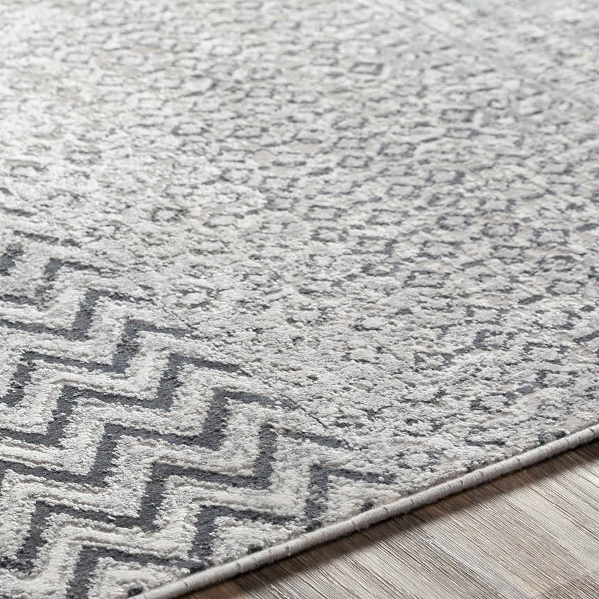 Close-up of the Rombauer Area Rug showing charcoal zigzags and light gray textured pattern on a wood floor. Texture