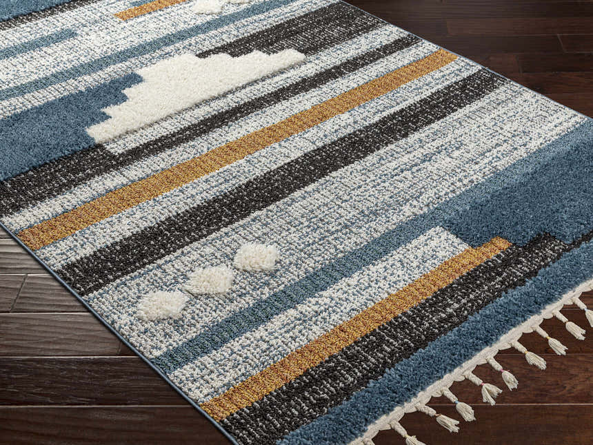 Close up of the Rosslare Area Rug featuring blue, camel, and black stripes with white tufted accents and tassels. Corner