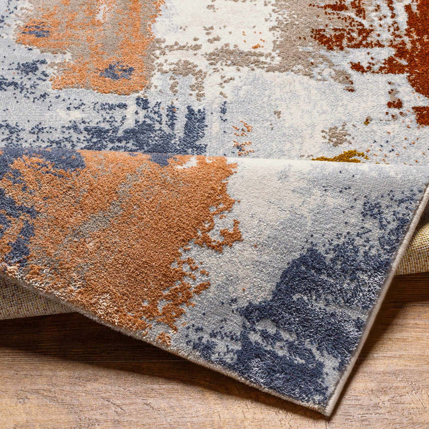 Close-up of the Rivers Area Rug showing brick red, dark blue, and light gray abstract pattern and soft texture. Fold