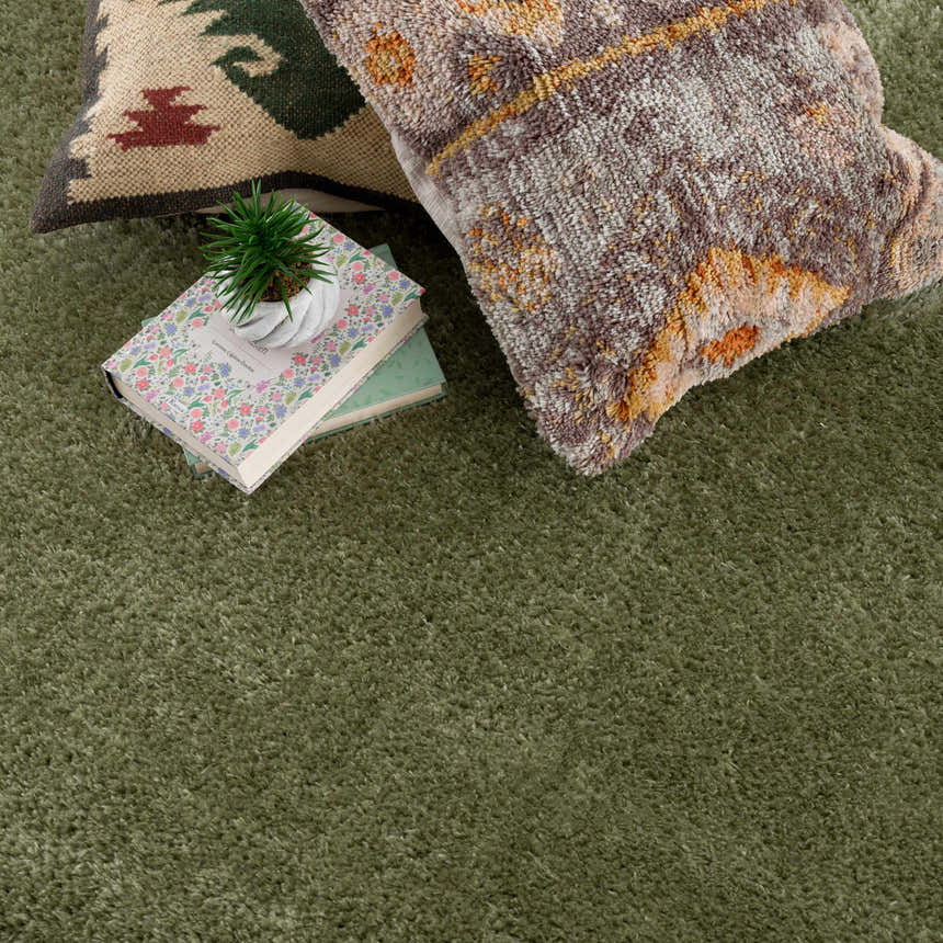 Close-up of the plush texture of the Heavenly Solid Green Plush Rug, styled with books and decorative pillows. Styleshot
