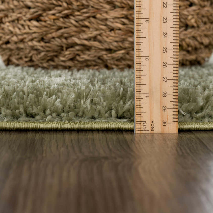 Close-up of the green Heavenly Solid Plush Rug showing the shag texture and pile height with a ruler for scale. Pile