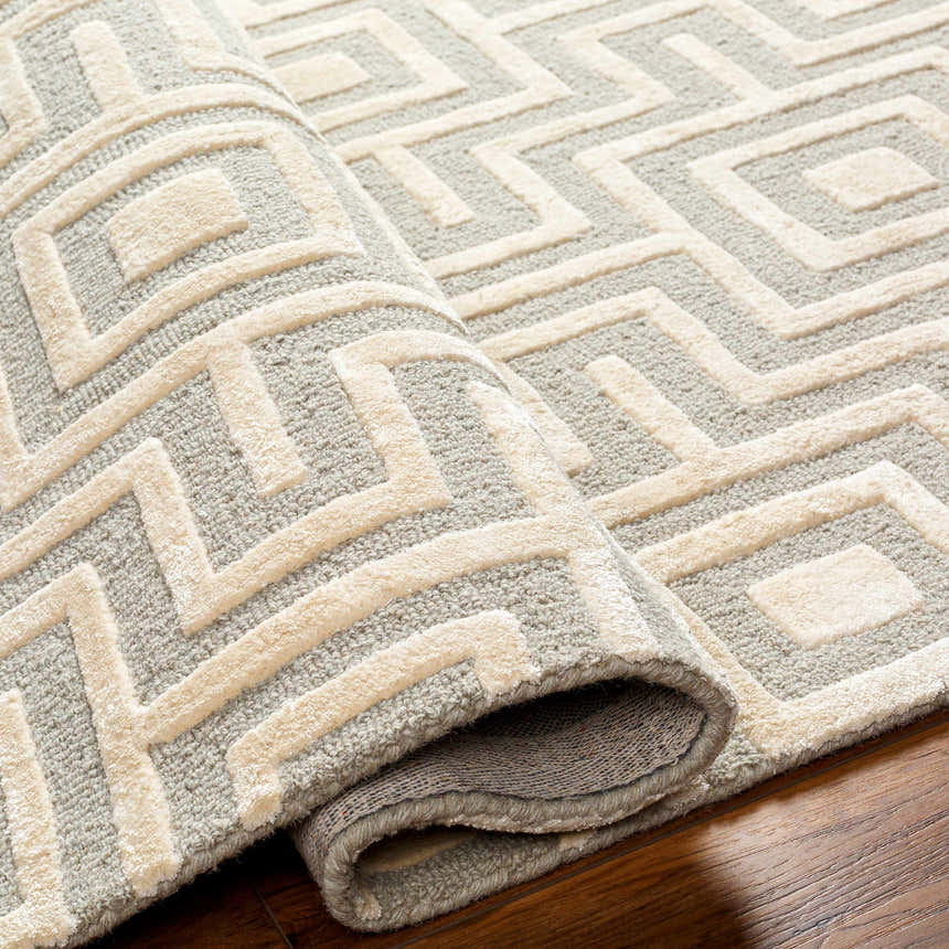 Close-up of the Fynn Beige Area Rug showing a geometric pattern in beige and gray, hand-tufted wool and viscose texture. Fold