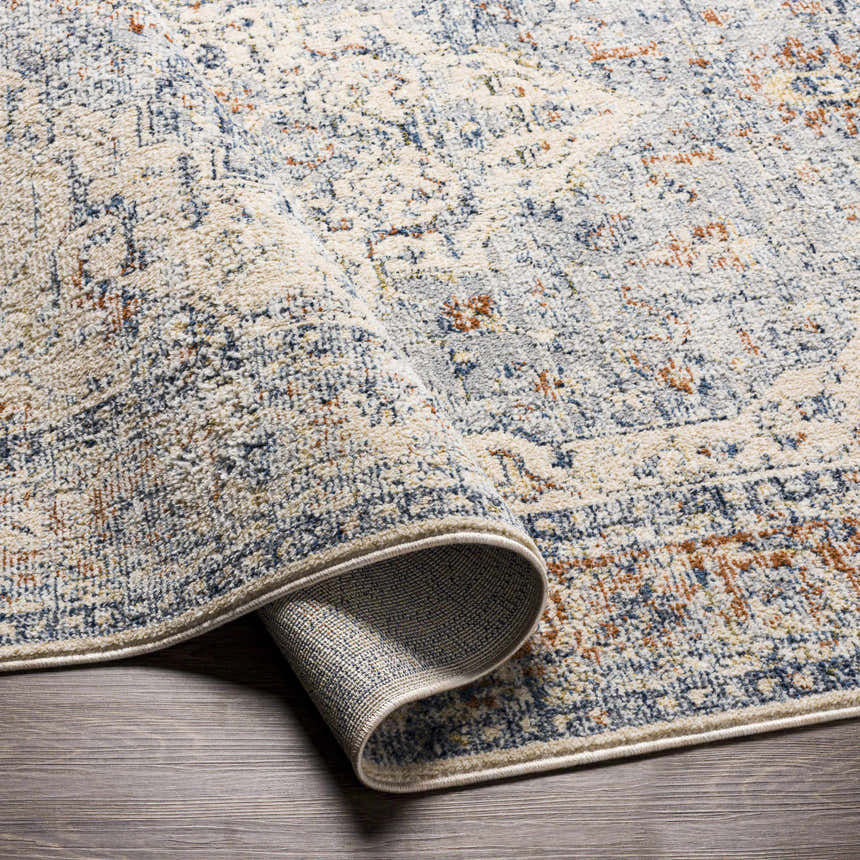 Close-up of the Salmo Area Rug showing its brick red, cream, and navy traditional pattern and soft, textured polyester material. Fold