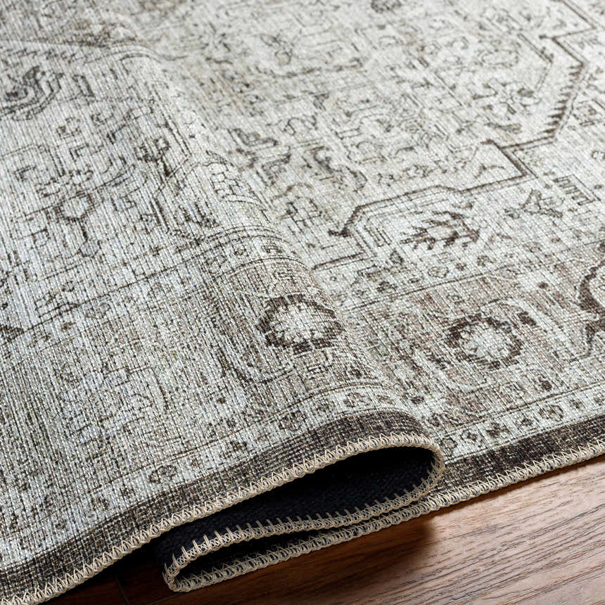 Close-up of the Anzu Washable Rug showing the traditional pattern, light gray and charcoal colors, and textured polyester material. Fold