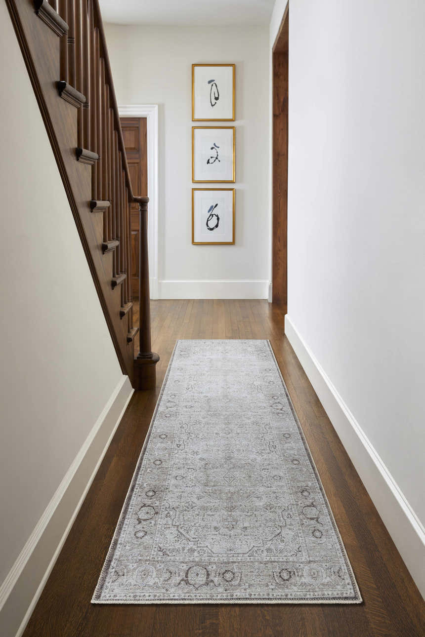 Hallway with wood floors and stairs featuring a gray Anzu Washable Rug runner, framed art, and white walls. Roomscene-Runner