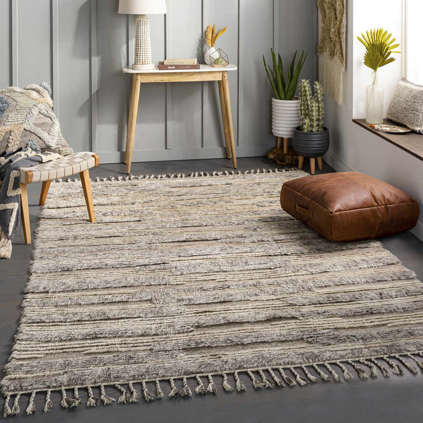 Living room scene with the textured Saundersfoot Area Rug in charcoal, gray, and beige. Bohemian style with a leather pouf and wood accents. Roomscene-Rectangle