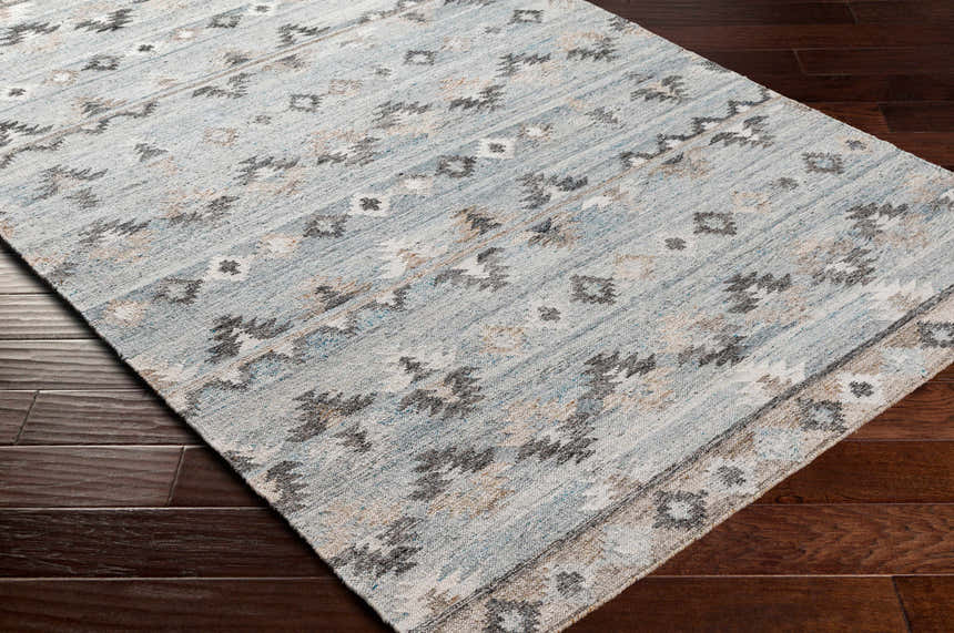 Close-up of the hand-woven Denna Area Rug. Features a Southwestern-inspired pattern in black, blue, brown, and white. Corner