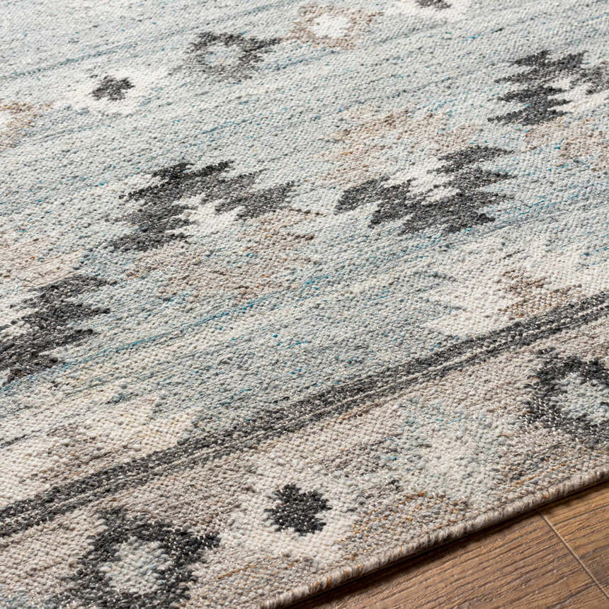 Close-up of the hand woven Denna Area Rug. Features a contemporary Southwestern pattern in black, blue, brown, and white. Texture