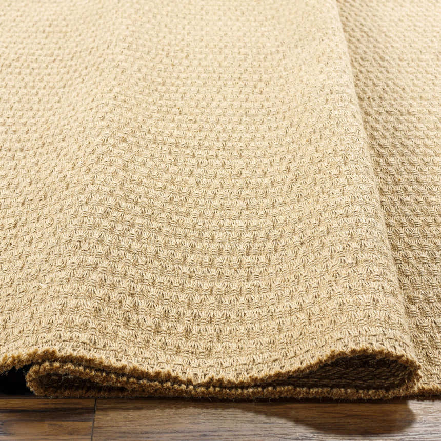Close-up of the camel Kimi Jute Area Rug showing its woven texture and jute fibers on a wood floor. Clearance rug. Fold