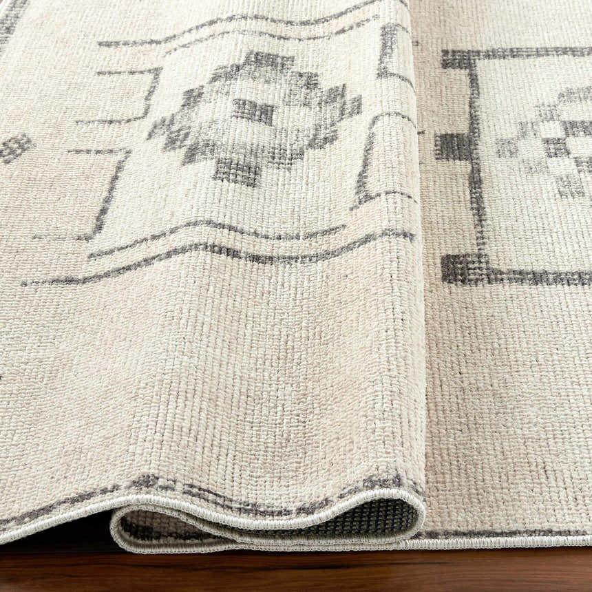 Close-up of Solana Medallion Charcoal rug by Livabliss x Becki Owens. Beige rug with gray medallion pattern and textured weave. Fold