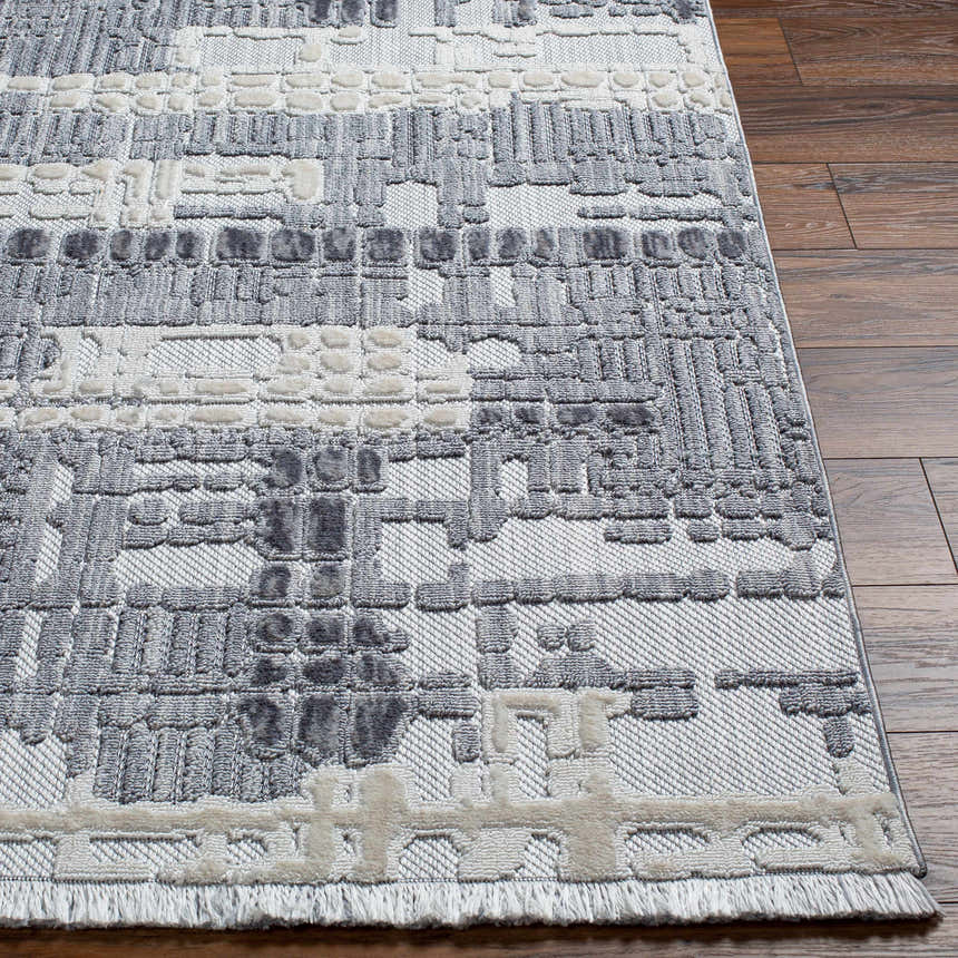 Close up of Bodhi Textured Saxony Rug. Gray, light gray, and charcoal hues with a geometric pattern and soft fringes. Front