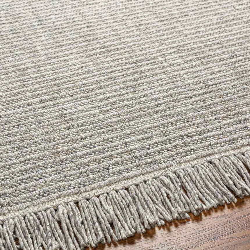 Close up of the Desma Taupe Area Rug showing its light gray color, textured weave, and knotted fringe detail. Texture