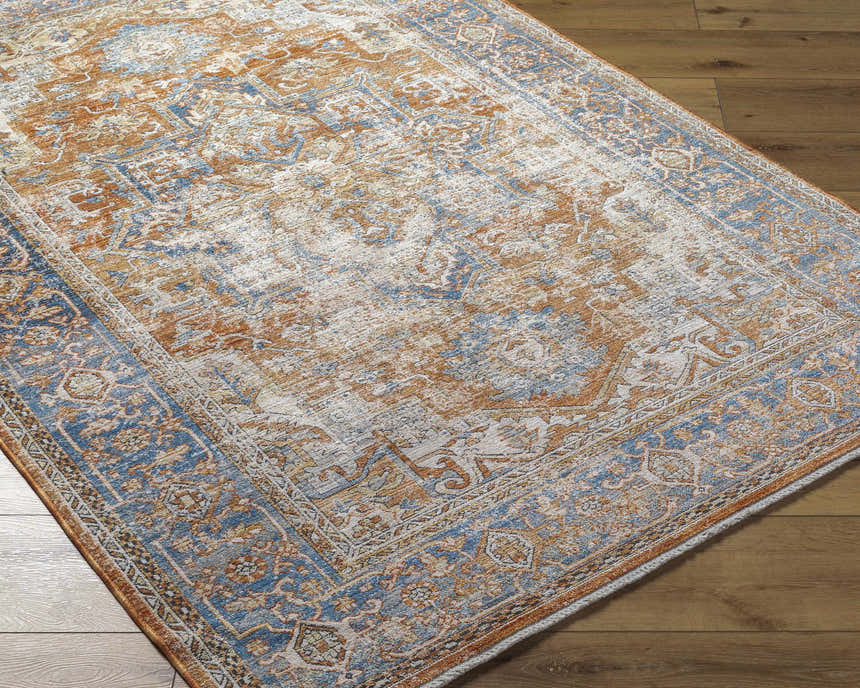 Close-up of the Basim Area Rug showing its traditional bone, copper, and blue farmhouse pattern and soft texture. Corner