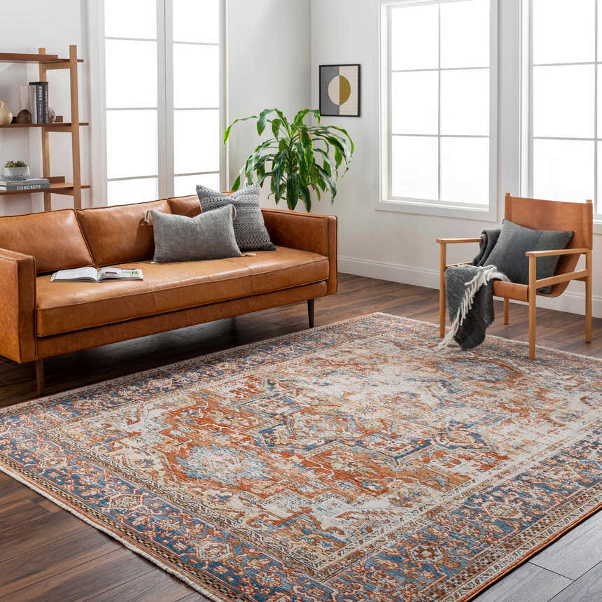 Living room scene with a Basim Area Rug in bone, charcoal, copper, and rust colors, styled with a leather sofa and wood chair. Roomscene-Rectangle